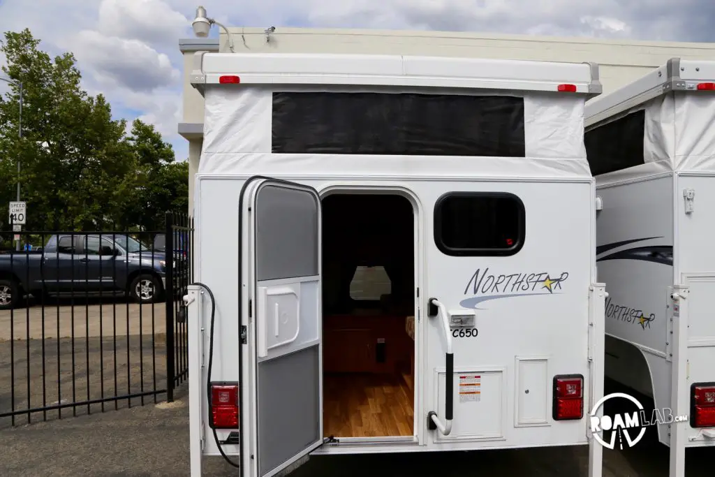 Here you can see the popup camper from the outside. The door is shorter so you have to duck through it and the top is expanded, with white fabric material that can keep some of the elements out but offers poor insulation and even poorer shade.