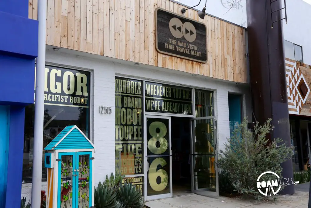 The exterior of the Time Travel Mart, complete with gold messages for Rigor the pacifist robot, TK brand robot toupees, five minute ago kits, robot milk, and more.