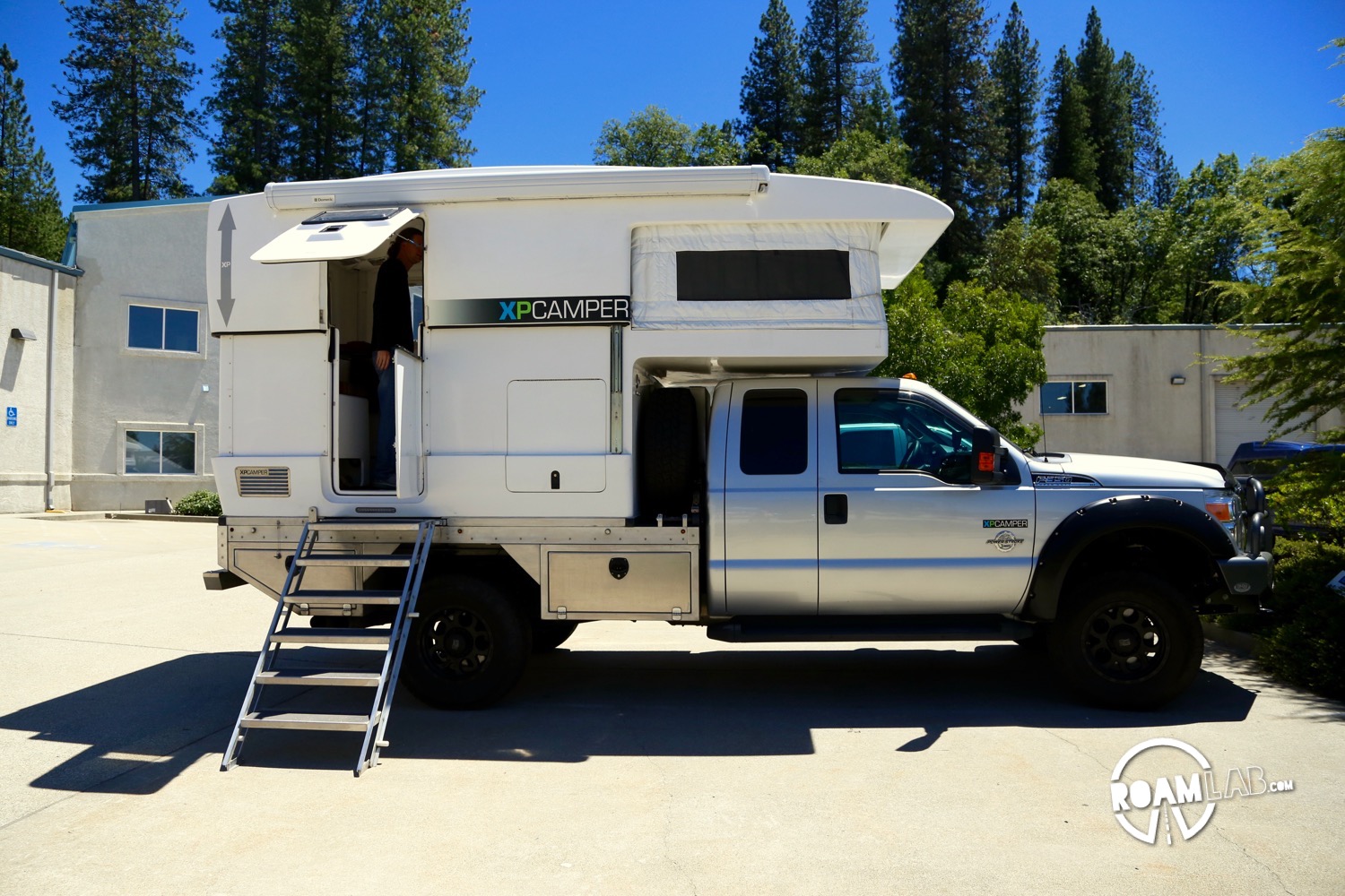 This is a fully expanded XP Camper. The section above the truck cab is fabric but everything else has hard siding. You can see a line along the center of the body where the top section slides over the bottom section when the camper is compressed. The side entrance allows a full width table with picture window at the back but means that this camper is not a slide in. The truck bed is converted to allow a full width camper. See the industrial metal base that is substituted for a truck bed.