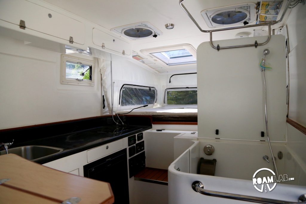 The interior reminds me a lot of the fiberglass interiors of boats. Walking around, I could almost be inside a little sail boat of my own. Just, this is a land ship. The bathroom section is open here. You can see the metal ring at the top that a shower curtain can be attached to. The back section folds down to act as the top of the bathroom section when not in use so it can be an extension of the counter. A nice addition when cooking.