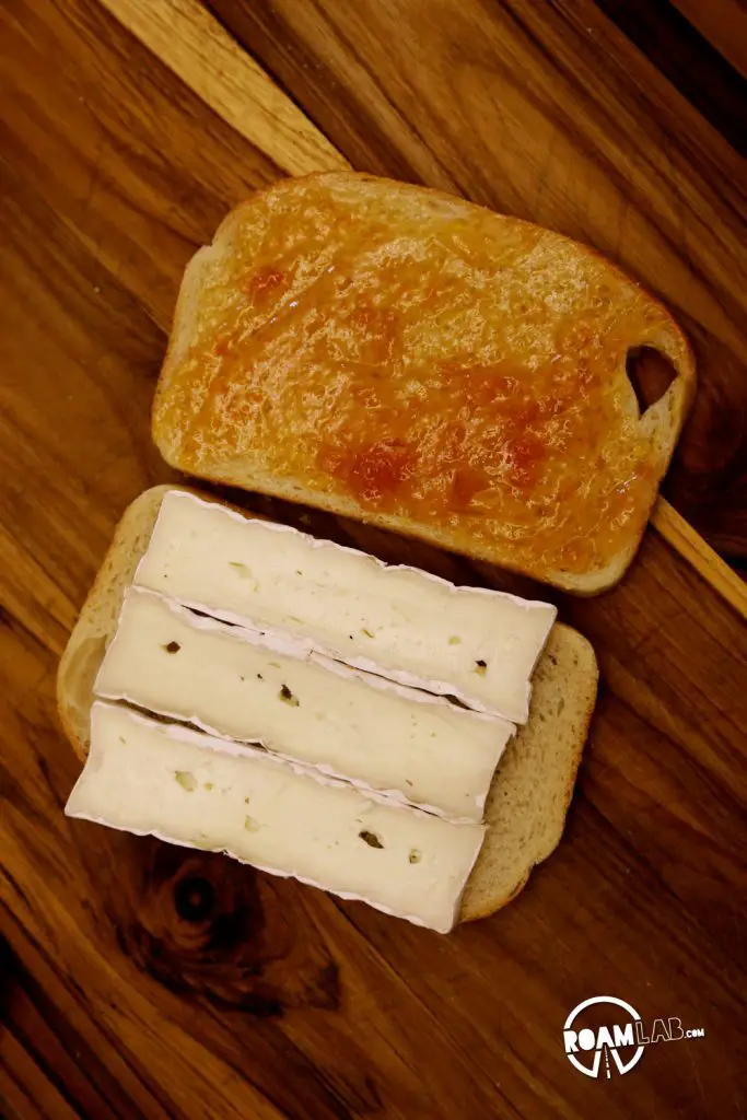 Spreading the the apricot jam and placing the sliced brie in place for a Glamper’s Bacon Brie Apricot Toasted Sandwich
