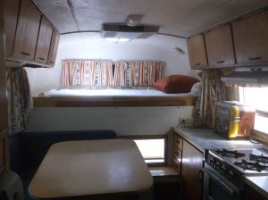 Interior shot of a 1970 Avion C11 truck camper capturing a dinette table, cabover bed, kitchen counter, and overhead storage.