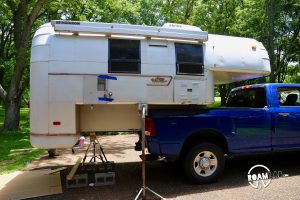 Removing a 1970 Avion C11 truck camper from the bed of a blue truck by jacking it up and driving the truck out from under the camper.