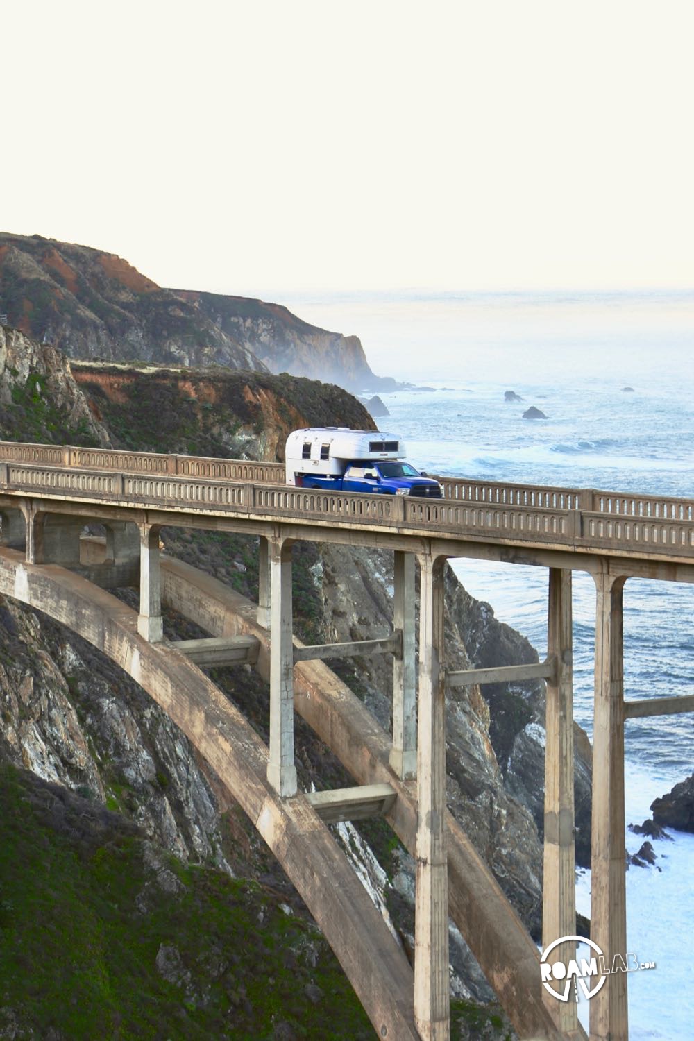 1970 Avion C11 truck camper crossing the Bixby Bridge in Big Sur with the ocean in the background.