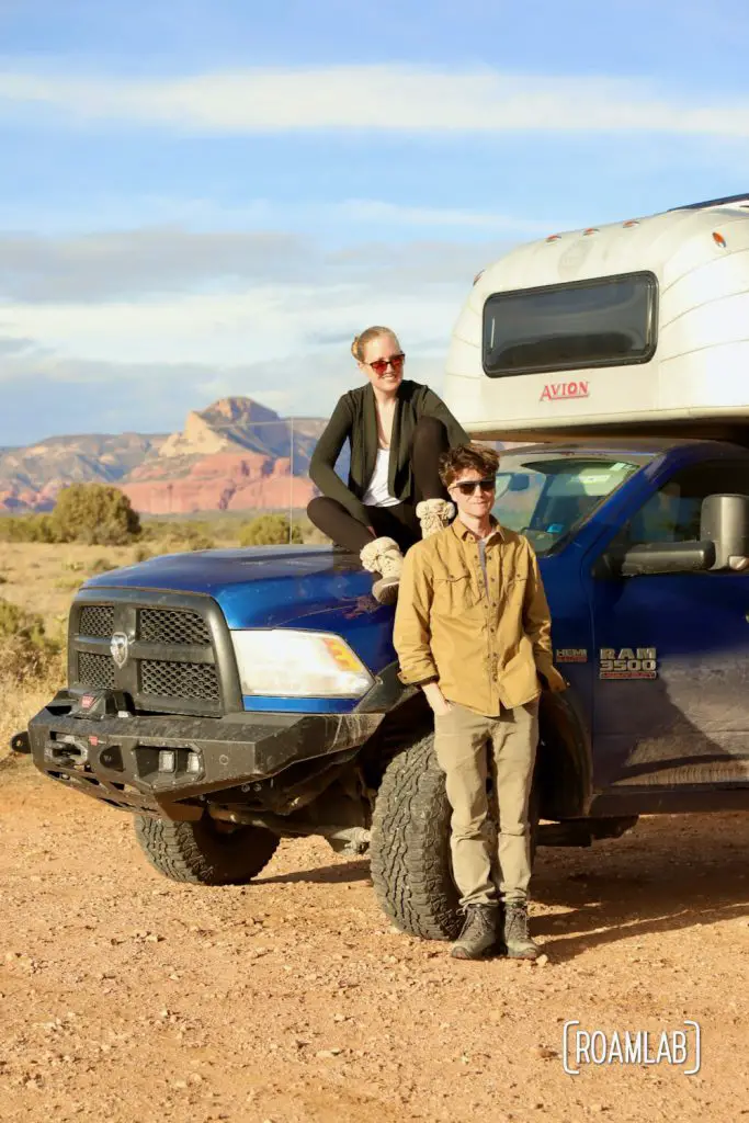 Man and woman sitting on the hood of a blue Ram truck with a 1970 Avion C11 truck camper in Sedona, Arizona.