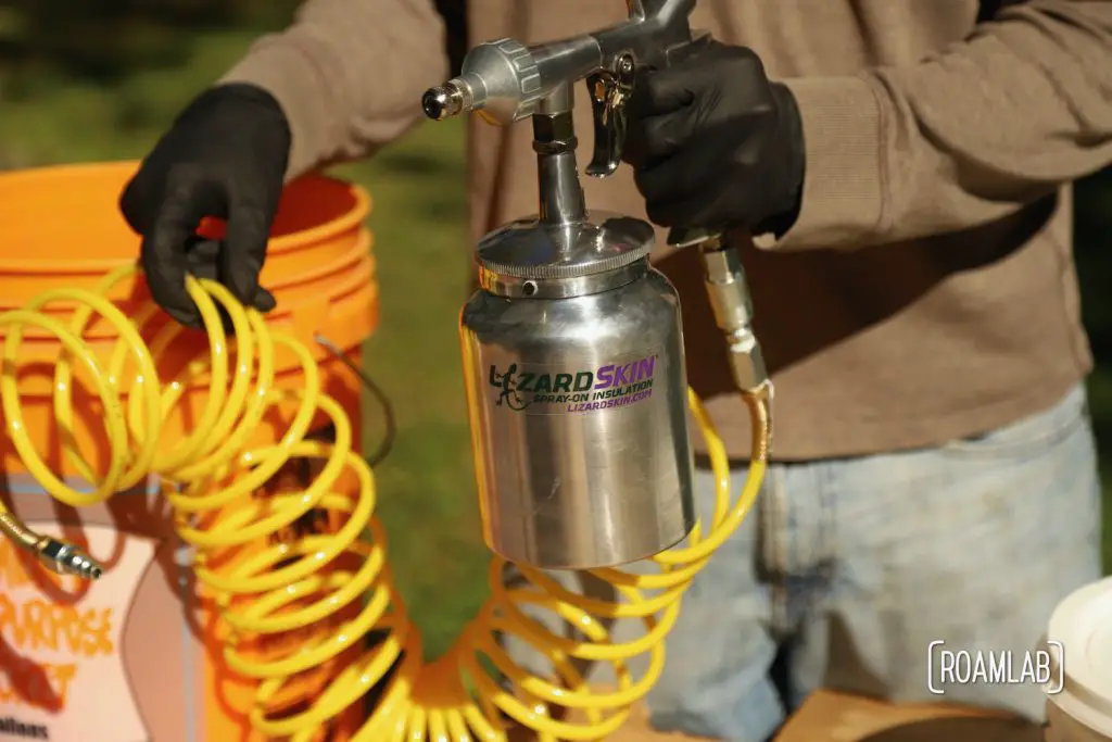 Gloved hand holding a spray gun with a Lizard Skin label.