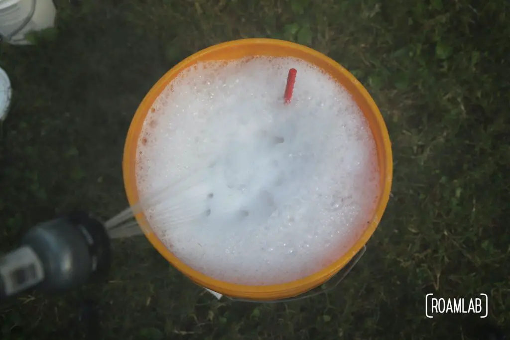 Filling an orange bucket with soaping water from a hose.