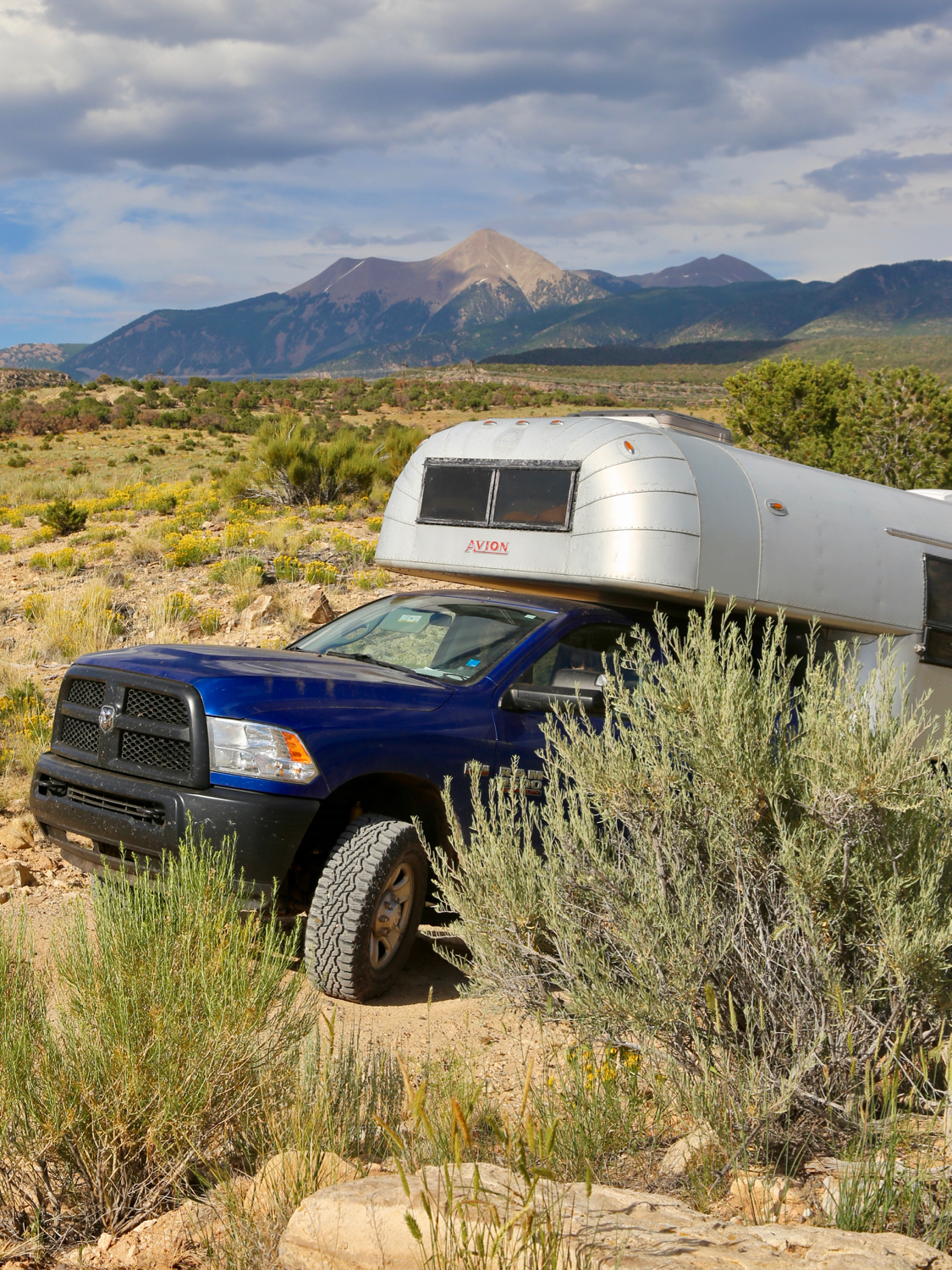 Aluminum truck camper on a blue truck peaking out between sage brush on a remote dirt road in the Utah Desert