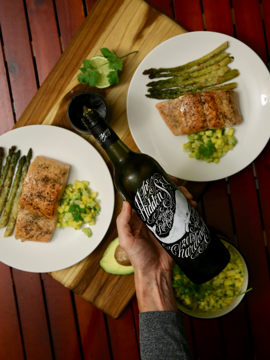 Hand pouring a bottle of wine with a salmon dinner