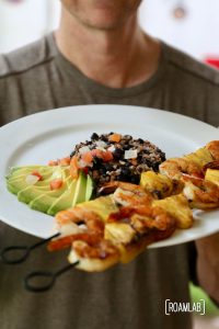Pineapple shrimp skewers with avocado, beans, rice, and pico de gallo.