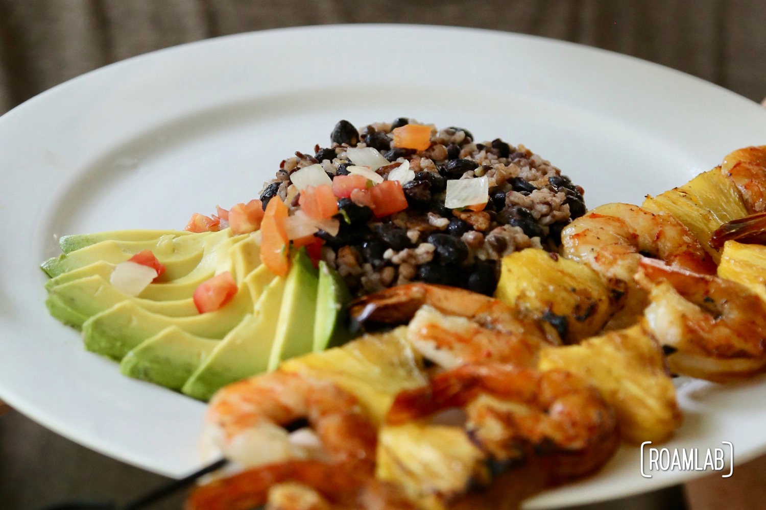 Pineapple shrimp skewers with avocado, beans, rice, and pico de gallo.