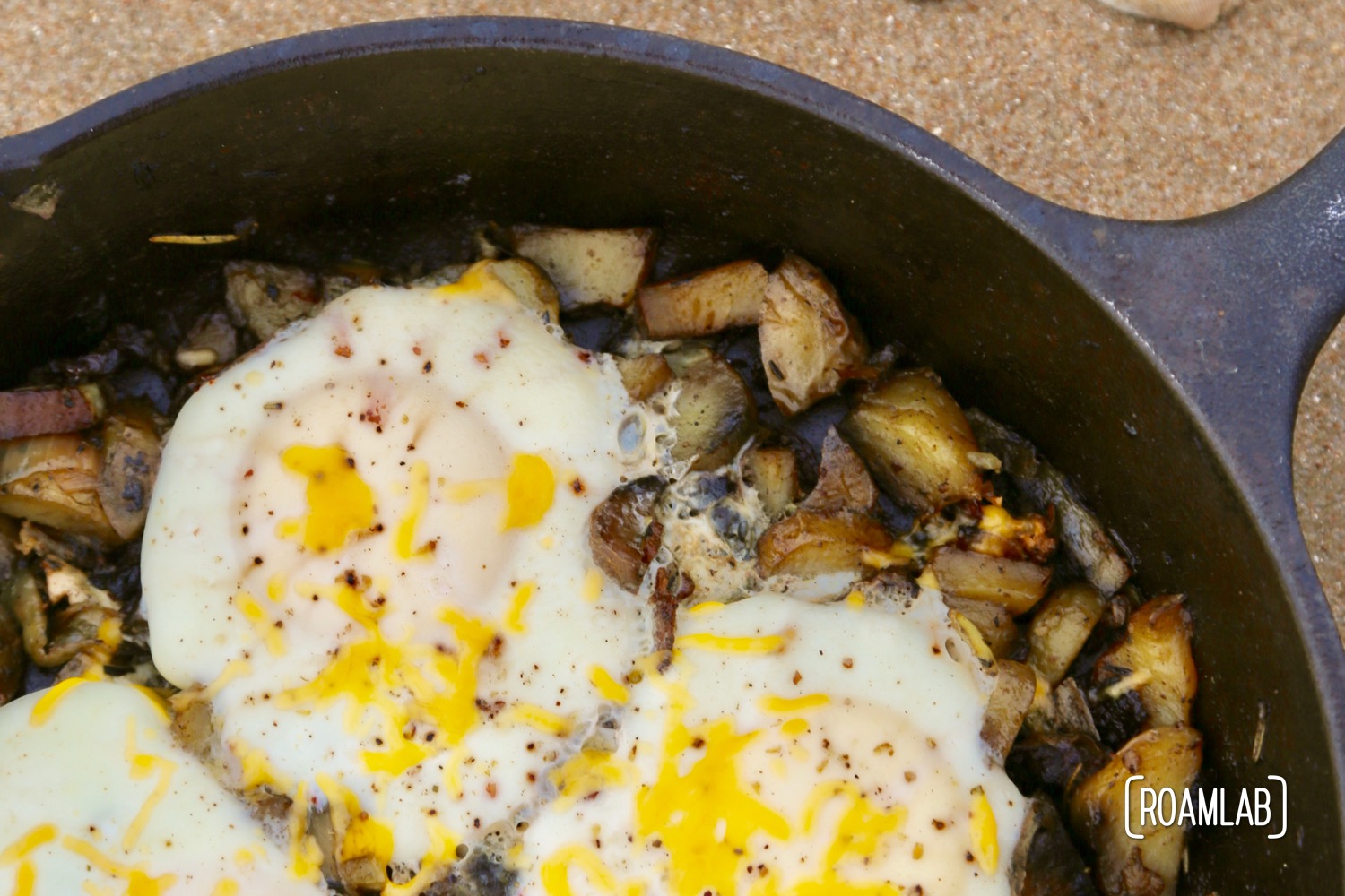 Cast iron skillet bacon and eggs hash on the beach.