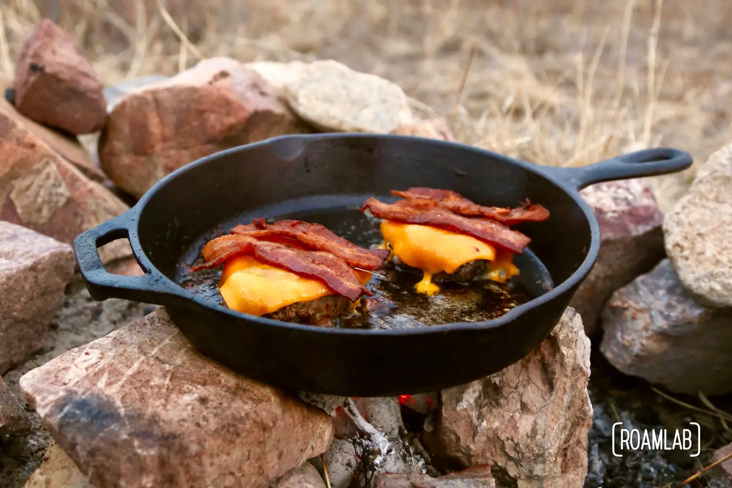 Bacon cheddar cheeseburger on a skillet over the coals.