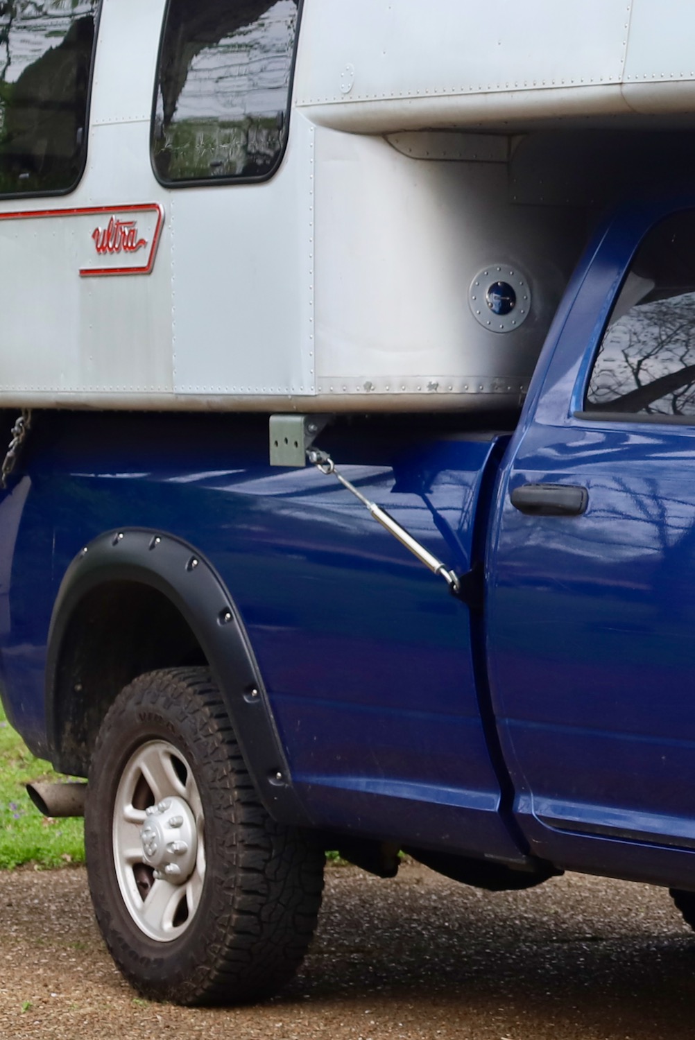 Truck camper secured to truck with discrete HappiJac tie-down and truck camper jack bracket connected with a spring loaded turnbuckle.