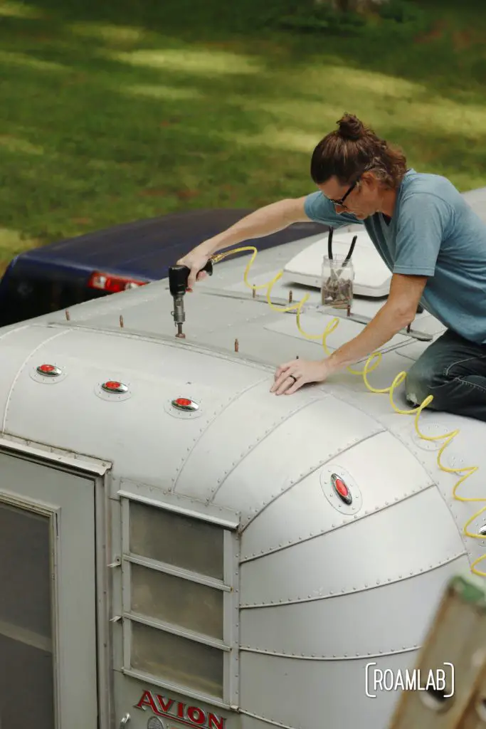 Man on roof of vintage 1970 Avion C11 truck camper riveting a piece of aluminum.