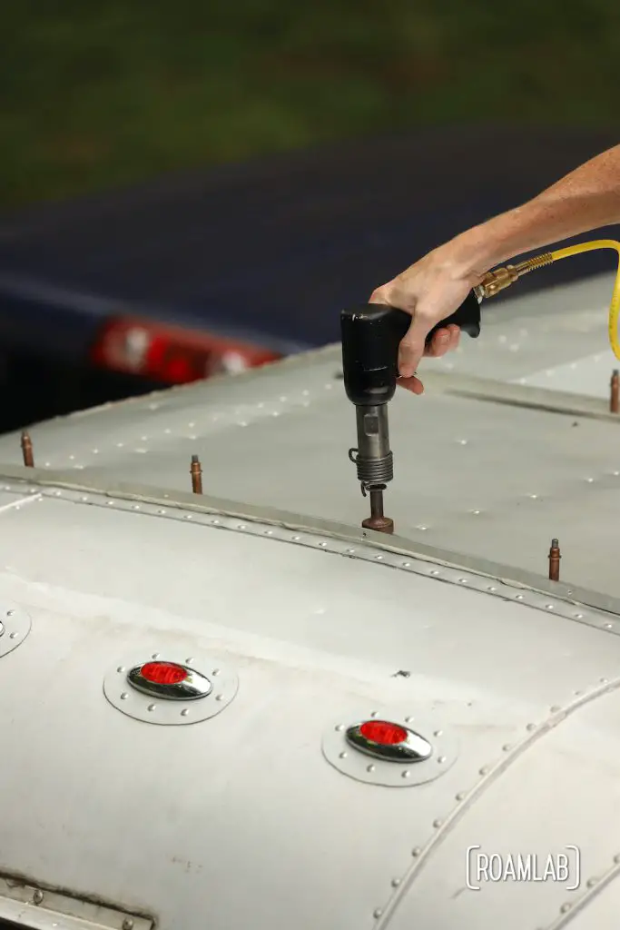 Hand holding a rivet gun to the roof of the aluminum 1970 Avion C11 truck camper.