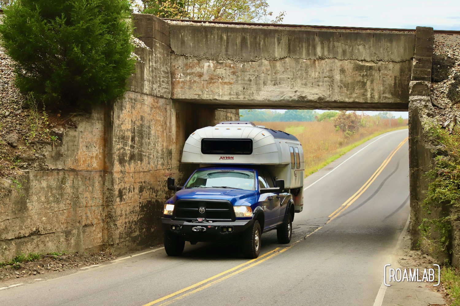 1970 Avion C11 truck camper driving under a railway bridge through a very low tunnel.