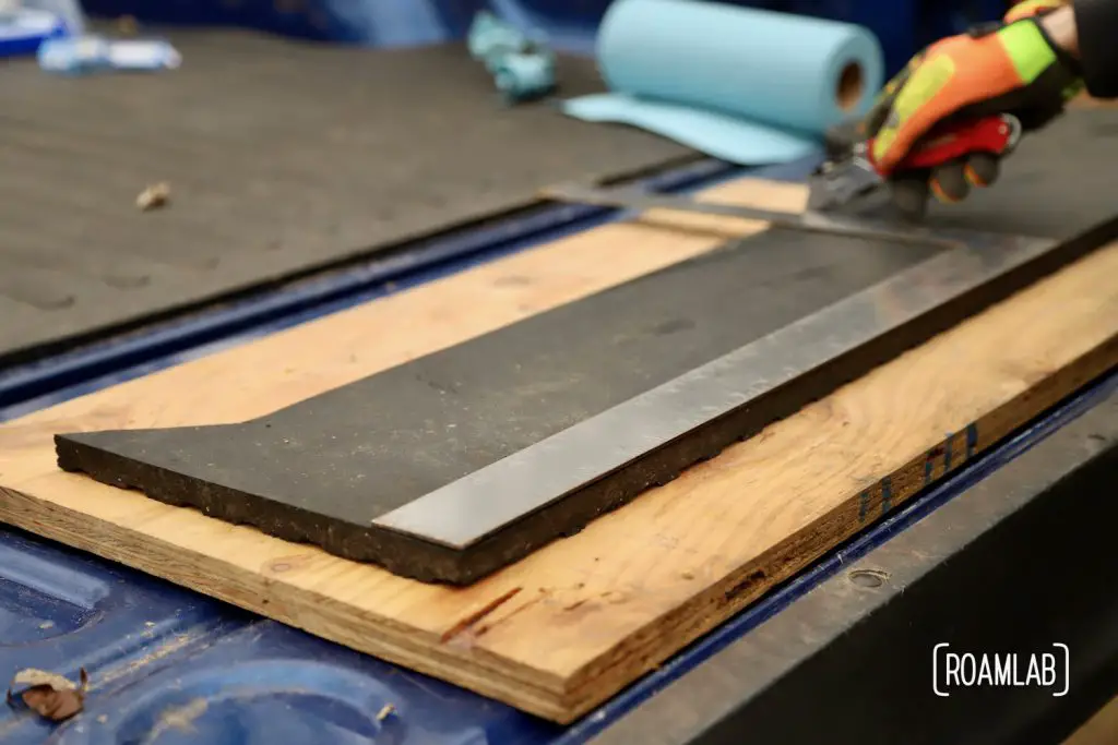 Using a right angle to measure and cut a thick piece of black rubber.