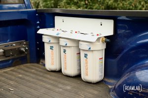 Large three canister water filtration system mounted to the passenger side of a truck bed.