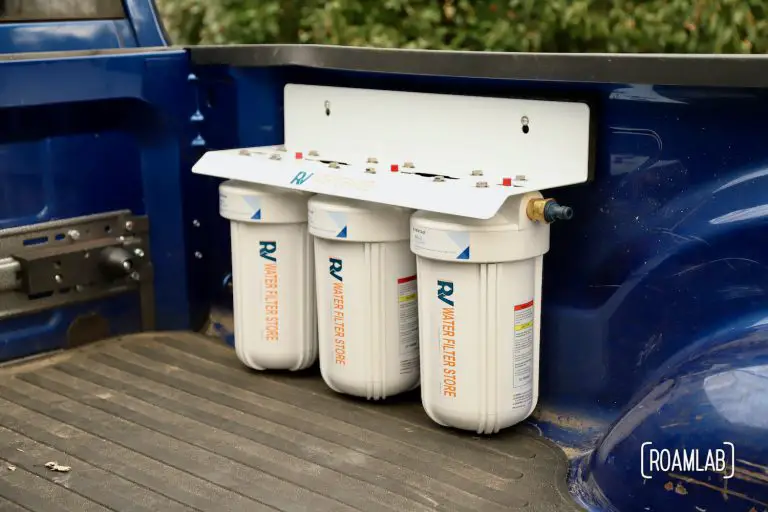Large three canister water filtration system mounted to the passenger side of a truck bed.