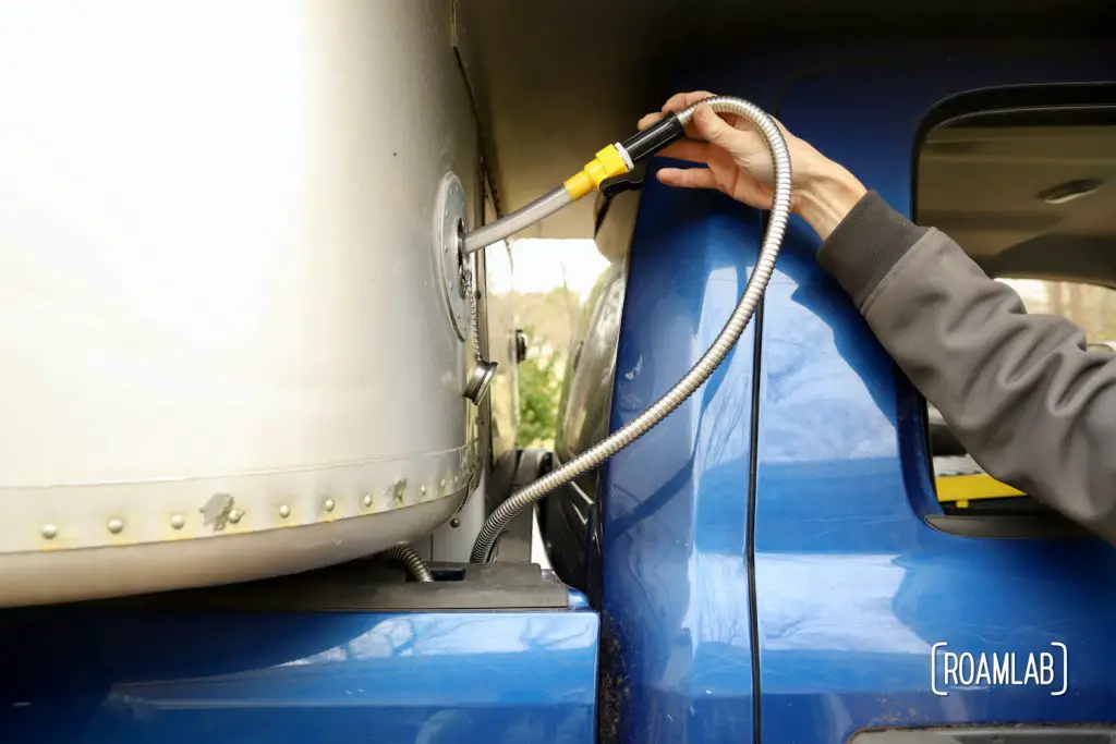 Hand holding a hose into the water intake opening on an aluminum truck camper.