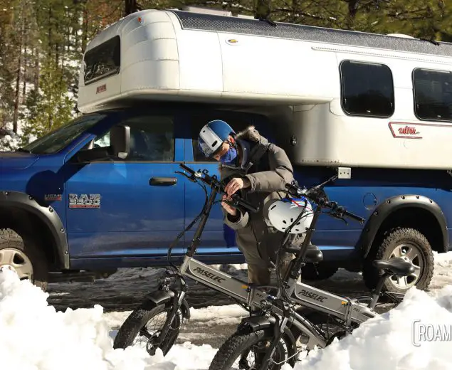 Man preparing bicycles in front of a 1970 Avion C11 truck camper.