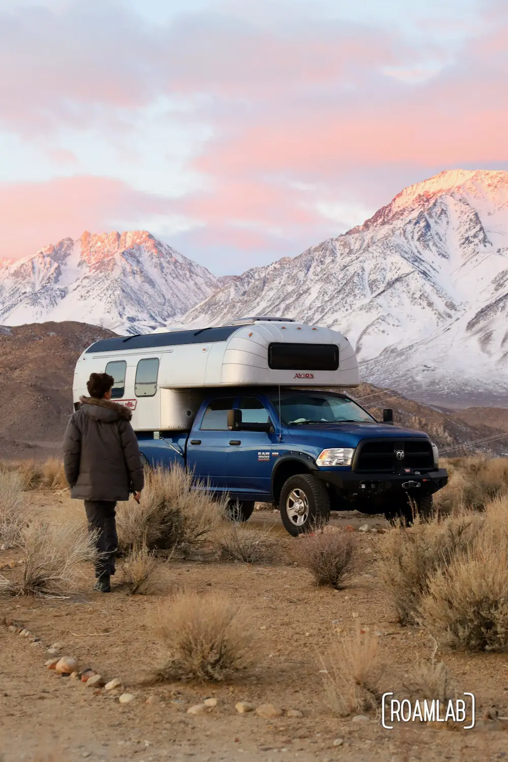 Man walking toward a 1970 Avion C11 truck camper with the pink tipped Sierra Nevada at dawn.