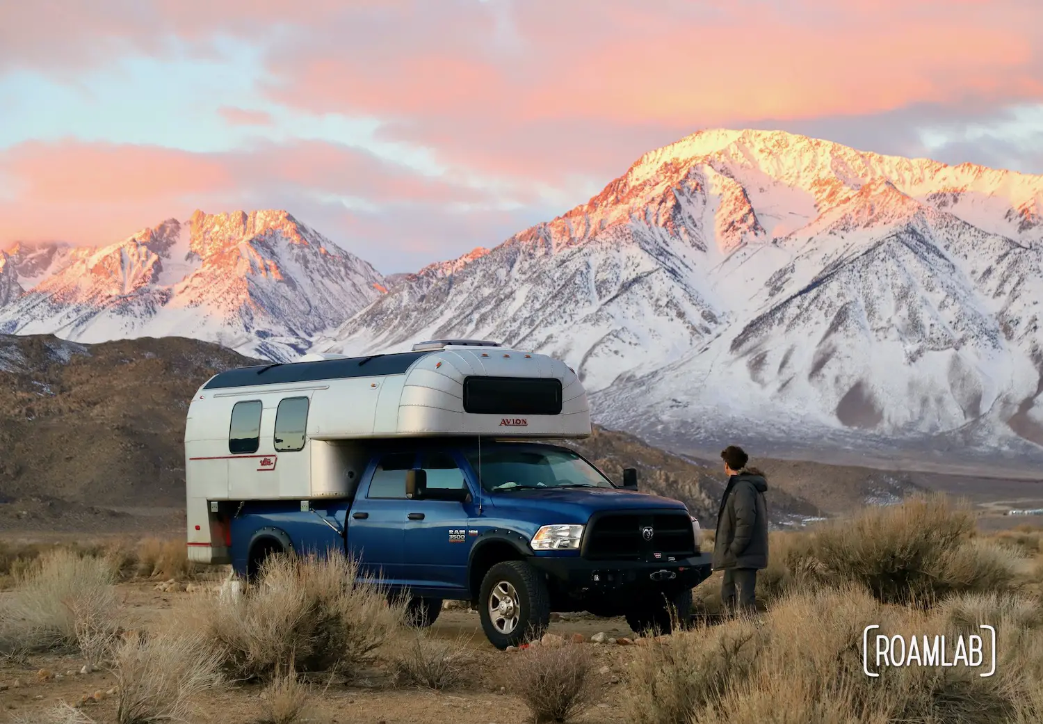Man walking toward a 1970 Avion C11 truck camper with the pink tipped Sierra Nevada at dawn.
