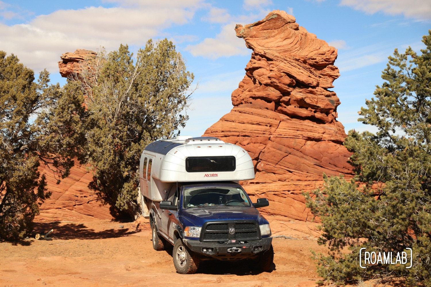 1970 Avion C11 truck camper parked next to a red rock hoodoo in Vermillion Hills National Monument.