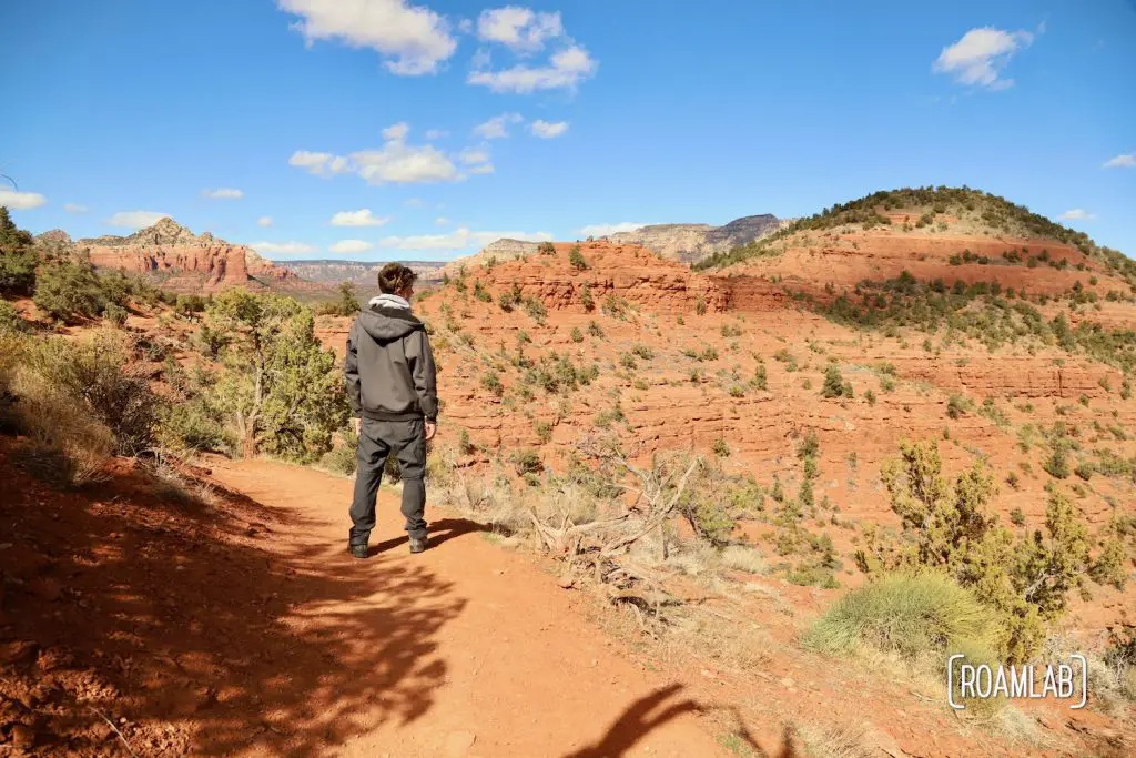 Man hiking along a red rock shelf on Airport Loop Trail in Sedona, Arizona.