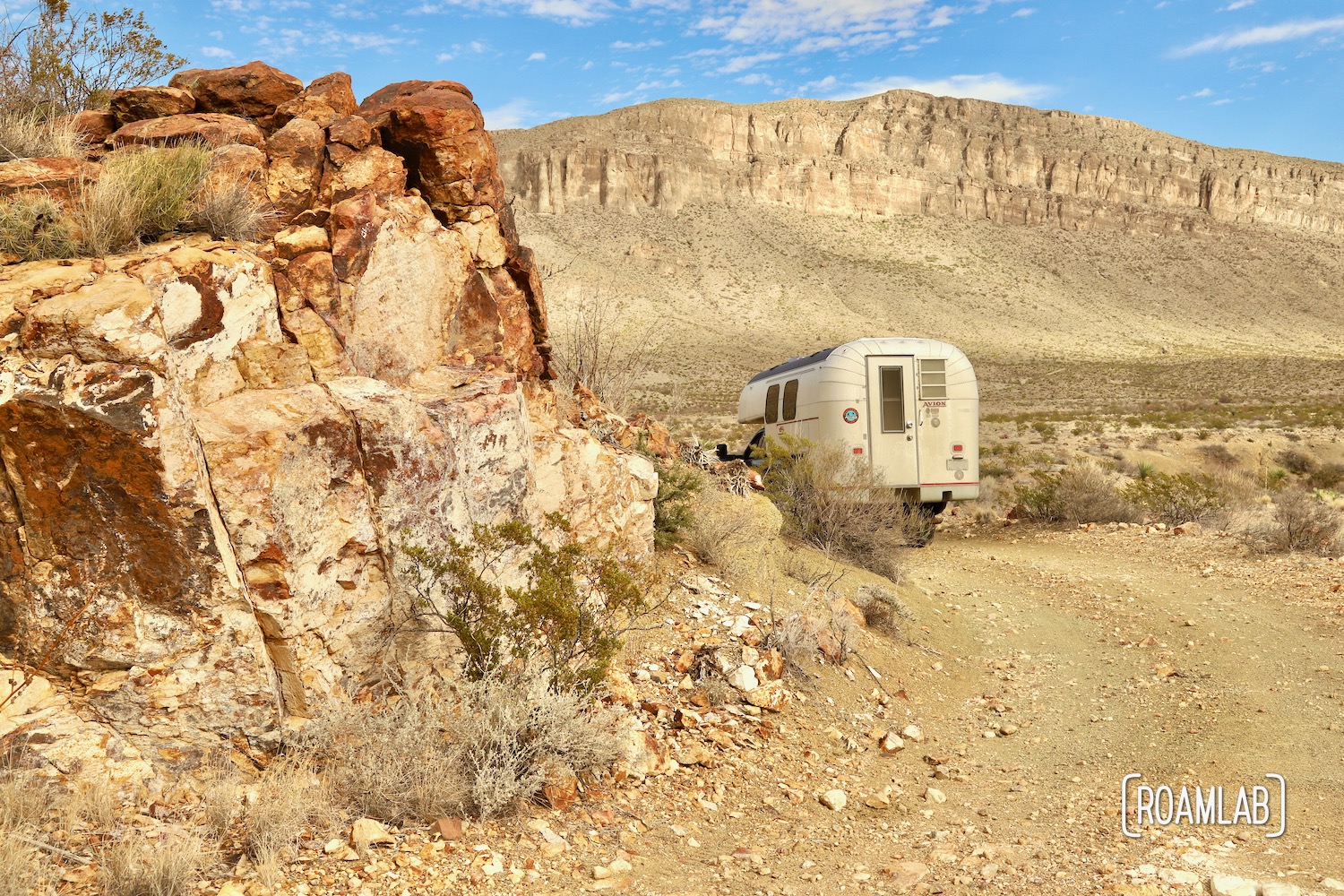 Avion C11 truck camper rounding colorful red rock formation and approaching the cliffs of the Alto Relex on the dirt Old Ore Road in Big Bend National Park, Texas.