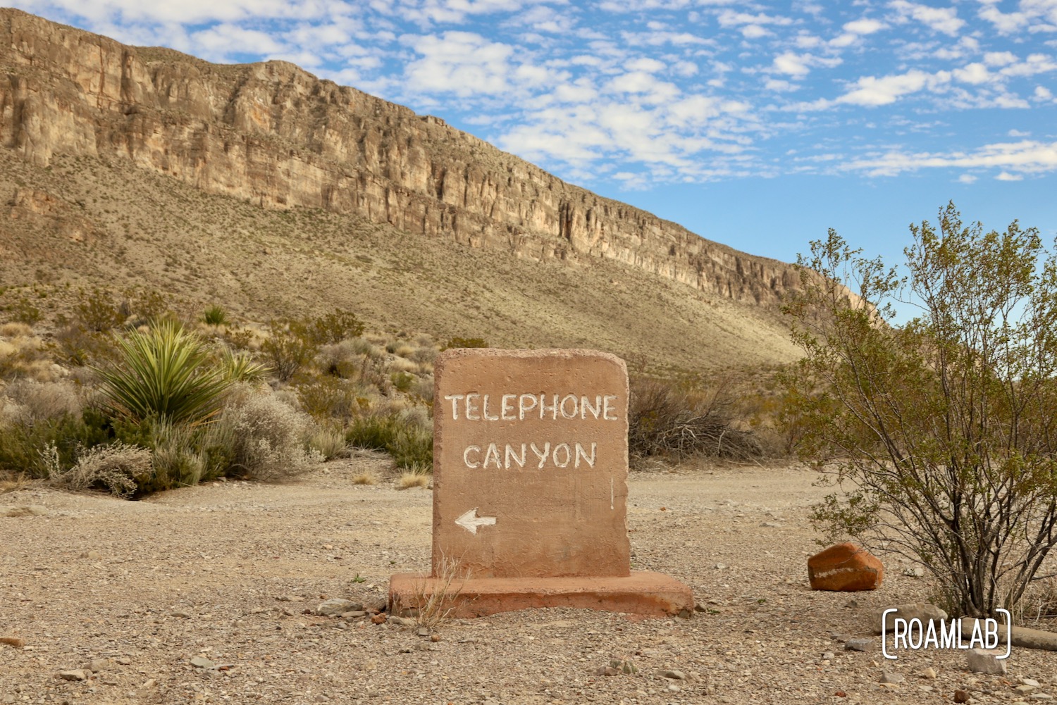 Grave stone like road marker for the Telephone Canyon Access Road off of Old Ore Road with cliffs and blue sky in the background.