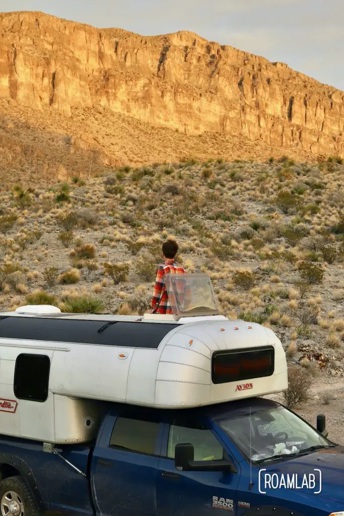 Man looking at golden cliffs through the roof hatch of a 1970 Avion C11 truck camper parked in the Telephone Canyon 1 campsite off of Old Ore Road in Big Bend National Park, Texas.