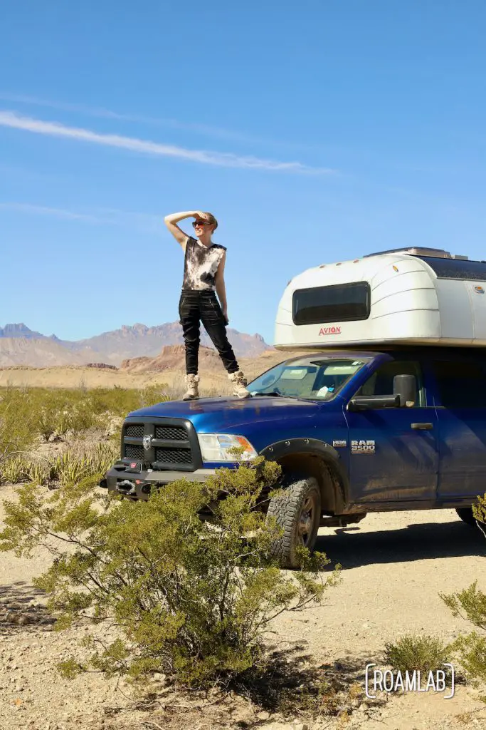 Woman standing on the hood of a 1970 Avion C11 truck camper parked at Fresno Campsite off River Road in Big Bend National Park, Texas.