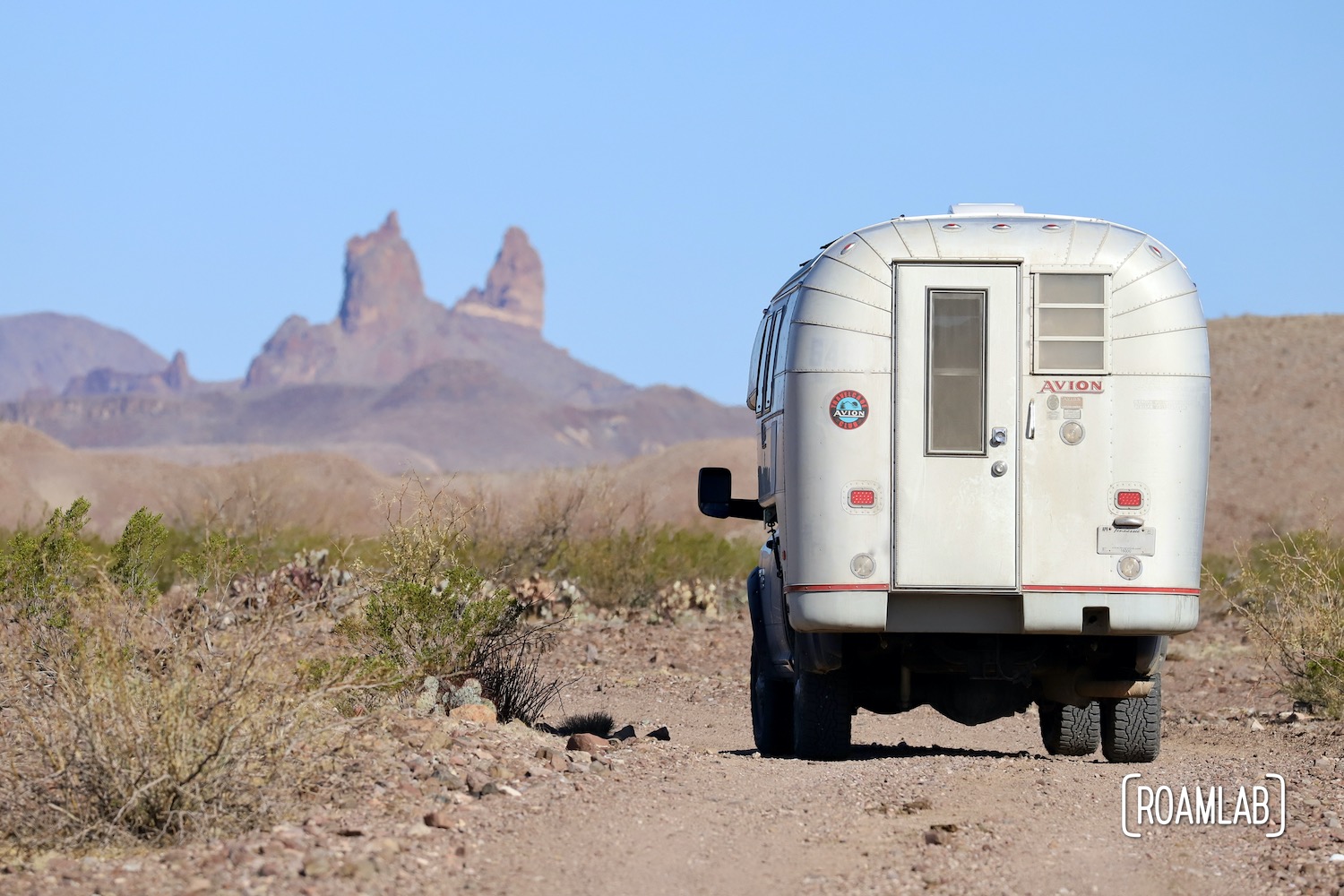 1970 Avion C11 truck camper driving down the dirt River Road towards the Mule's Ears rock formation in Big Bend National Park in southwest Texas.