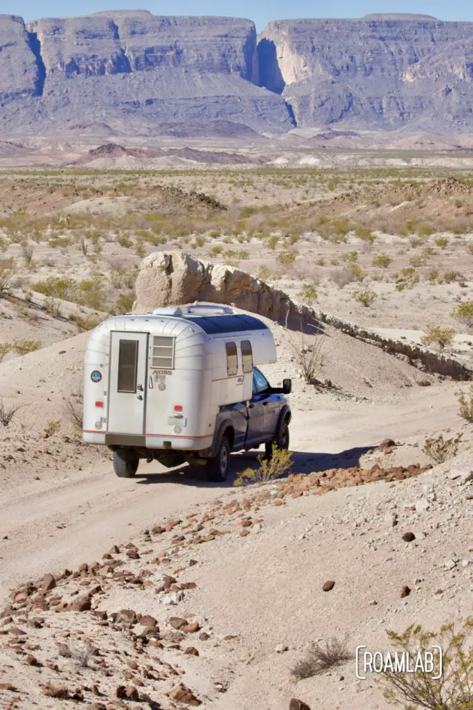 Vintage 1970 Avion C11 truck camper driving down a dirt road with purple mountains in the background along River Road in Big Bend National Park, Texas