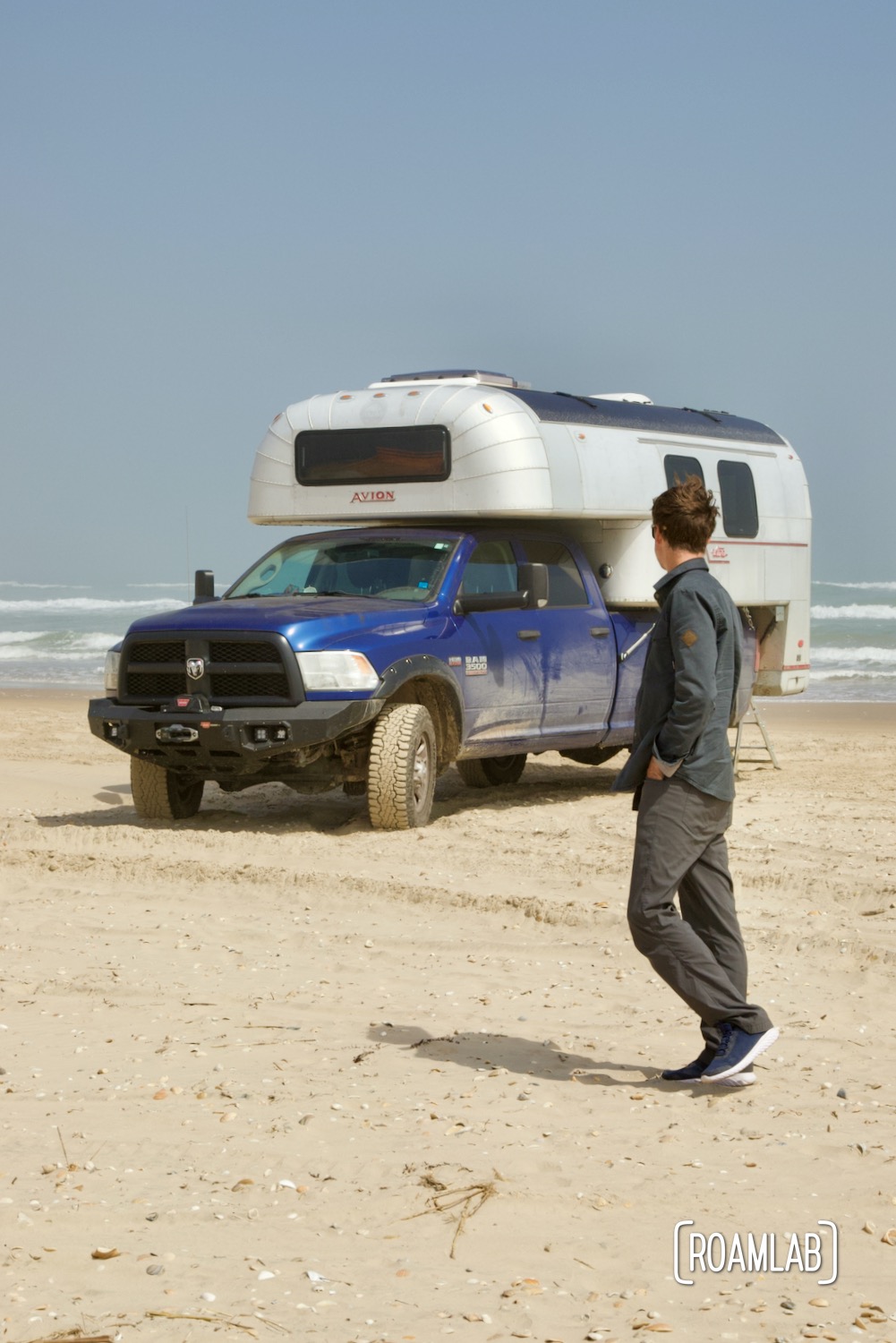 Man walking in front of a 1970 Avion C11 truck camper parked on the South Padre Island beach in Texas