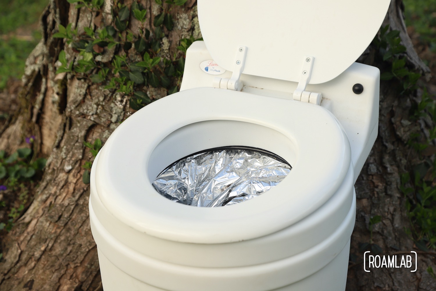 Laveo By Dry Flush toilet with cartridge installed, sitting in front of an ivy covered tree.