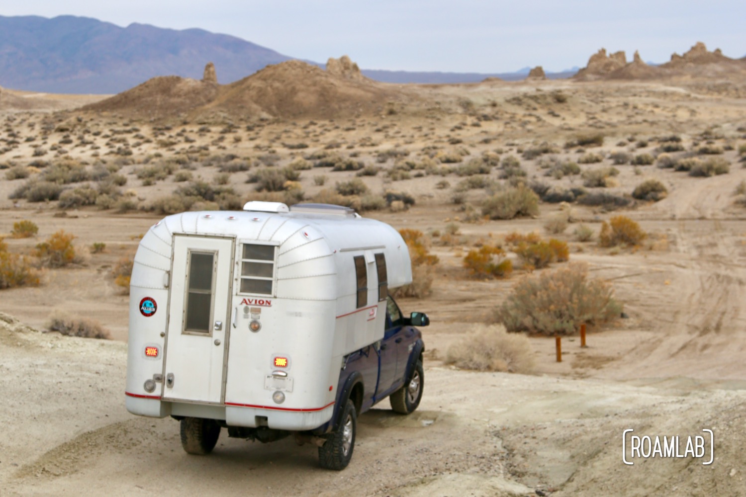 Aluminum 1970 Avion C11 truck camper driving down a dirt road in Trona Pinnacles Wilderness in south east California.