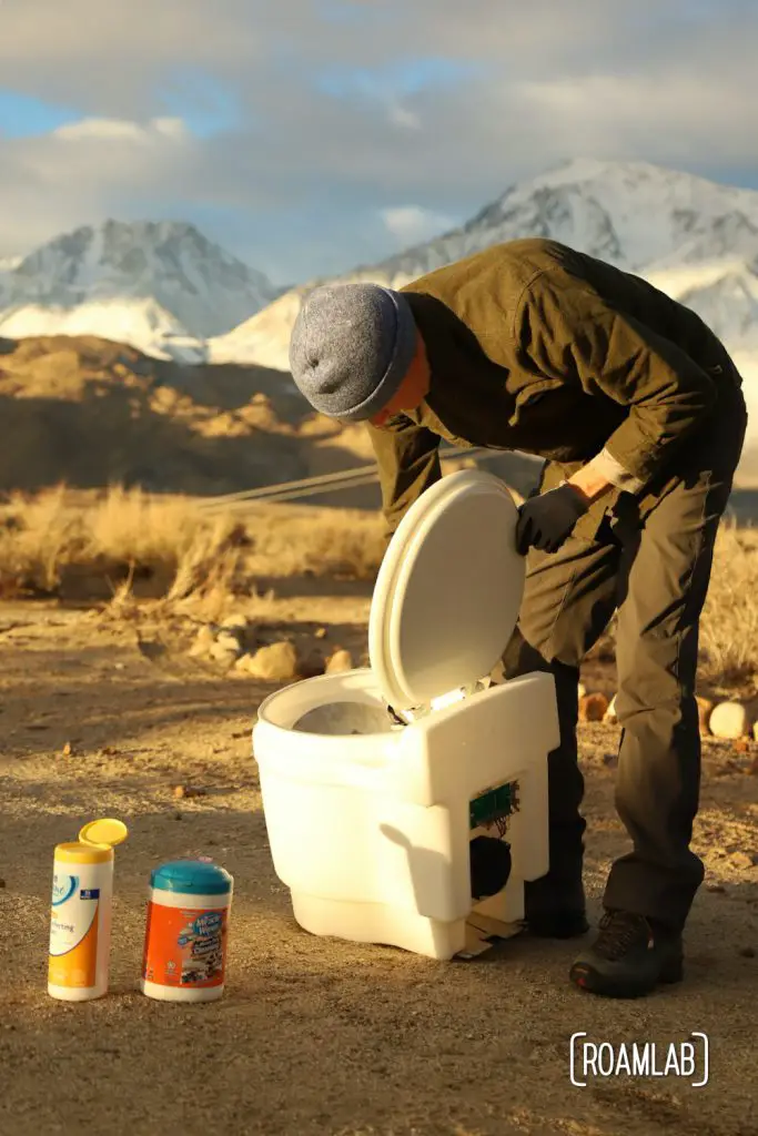 Man cleaning a dry flush toilet with the Sierra Nevada in the background.