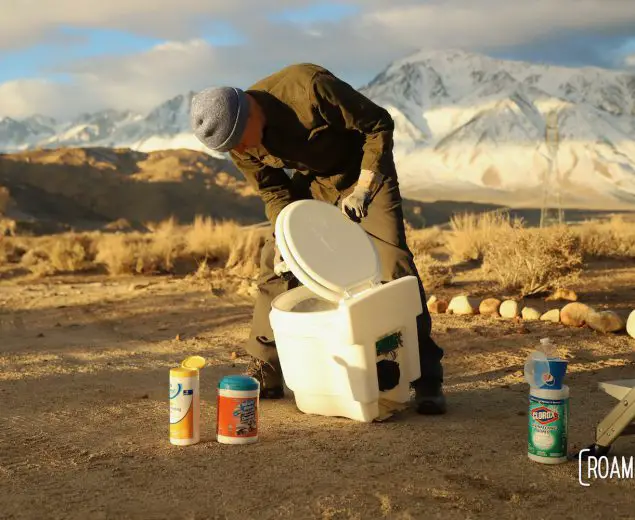 Man cleaning a dry flush toilet with the Sierra Nevada in the background.