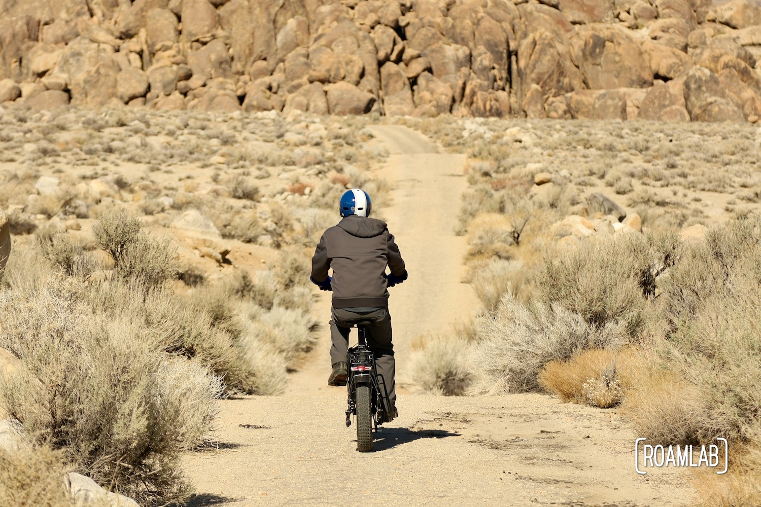 Man biking down a rough sandy trail toward a pile of boulders in the Alabama Hills.