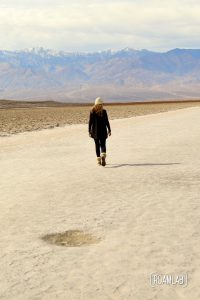 Woman in black walking out on a wide sandy trail of a dry lake bed in Death Valley's Badwater Basin.