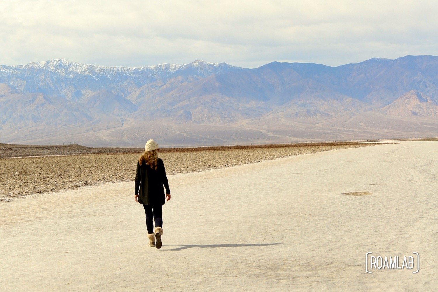 Woman in black walking out on a wide sandy trail of a dry lake bed in Death Valley's Badwater Basin.