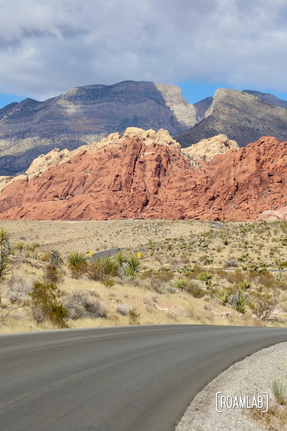 A paved road winding toward red rock cliffs.
