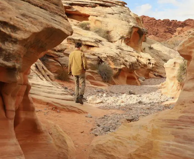 Man wandering through a red sandstone wash in White Domes Trail in Nevada's Valley of Fire State Park.