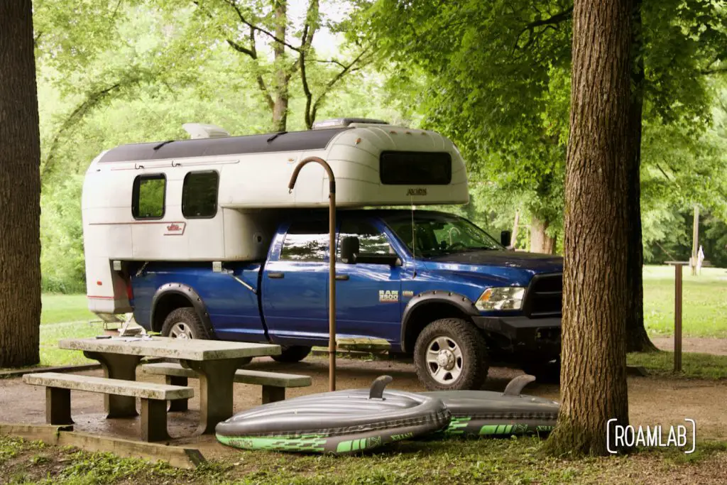 1970 Avion C11 truck camper in parked at the Houchin Ferry Campground in Mammoth Caves National Park with a picnic table and kayaks in the foreground.