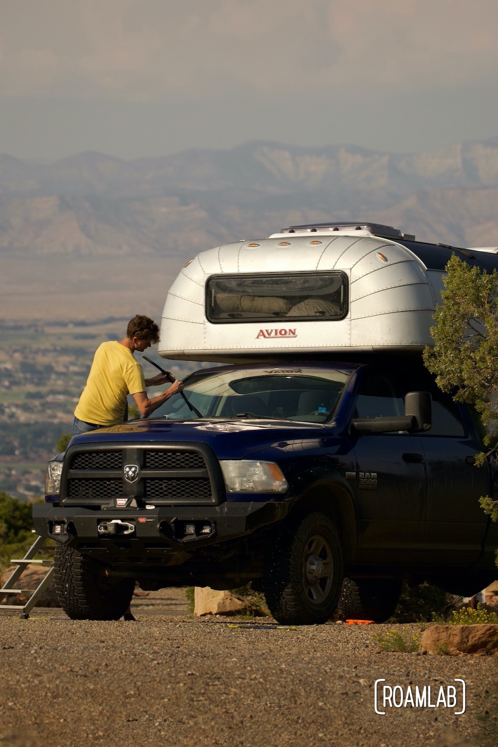 Man sitting on the hood of a blue truck with a 1970 Avion C11 truck camper at Saddlehorn Campground in Colorado National Monument.