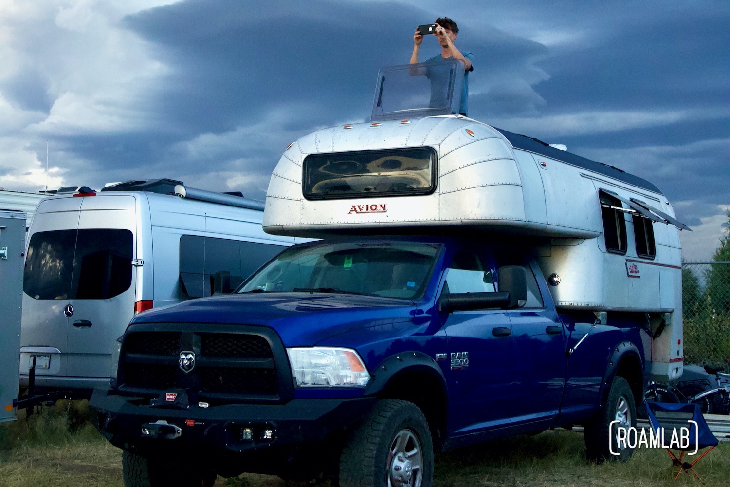 Man Looking out a room hatch at a 1970 Avion C11 truck camper as heavy storm clouds roll in.