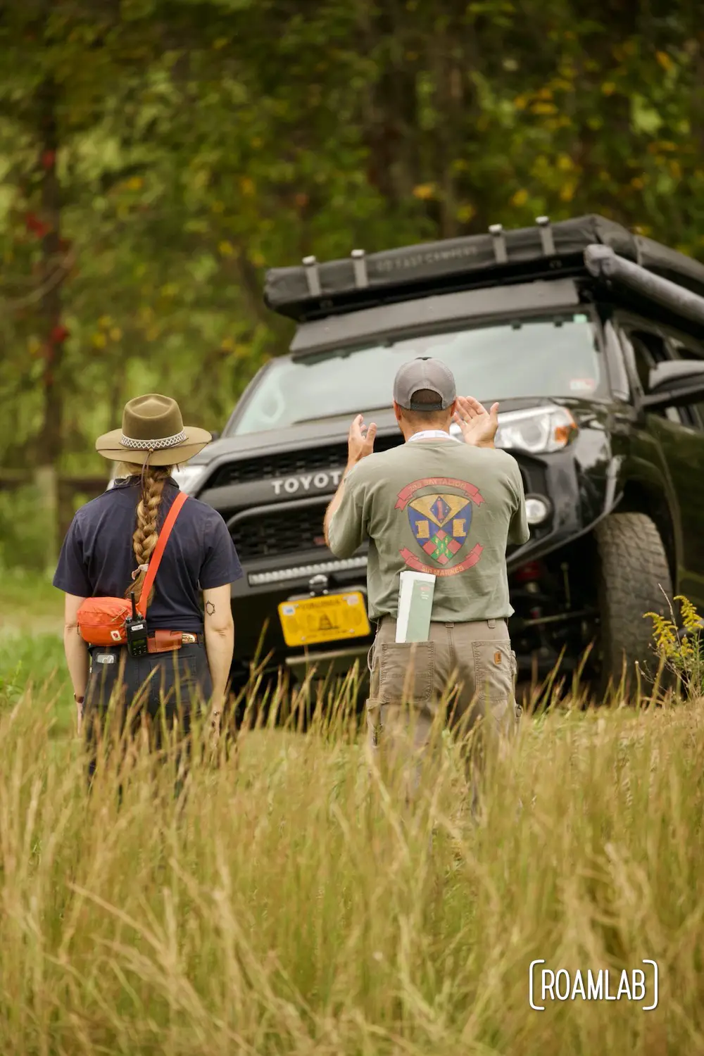 Man gesturing at an oncoming black Toyota on a rough dirt course at Overland Expo East 2021 in Arrington, Virginia.